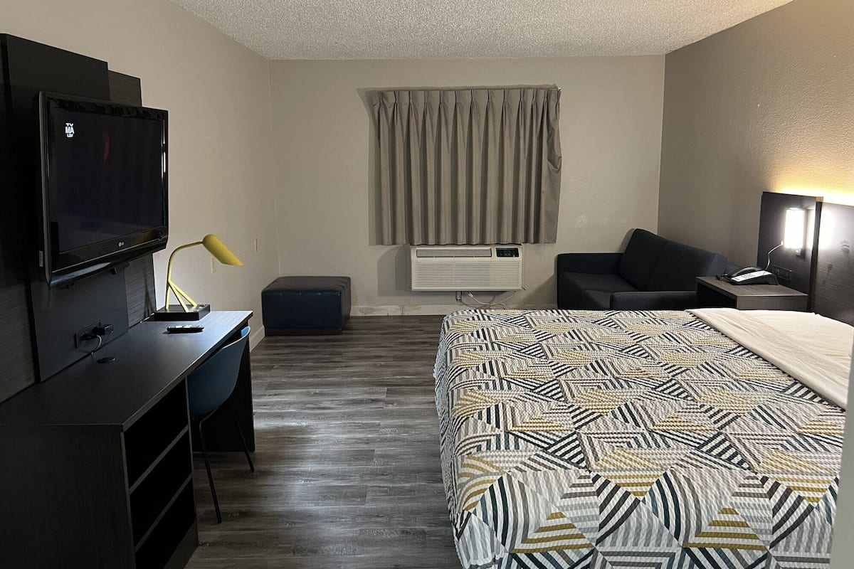Habitación de hotel con cama, escritorio con televisor, una silla, sofá, aire acondicionado y lámpara.