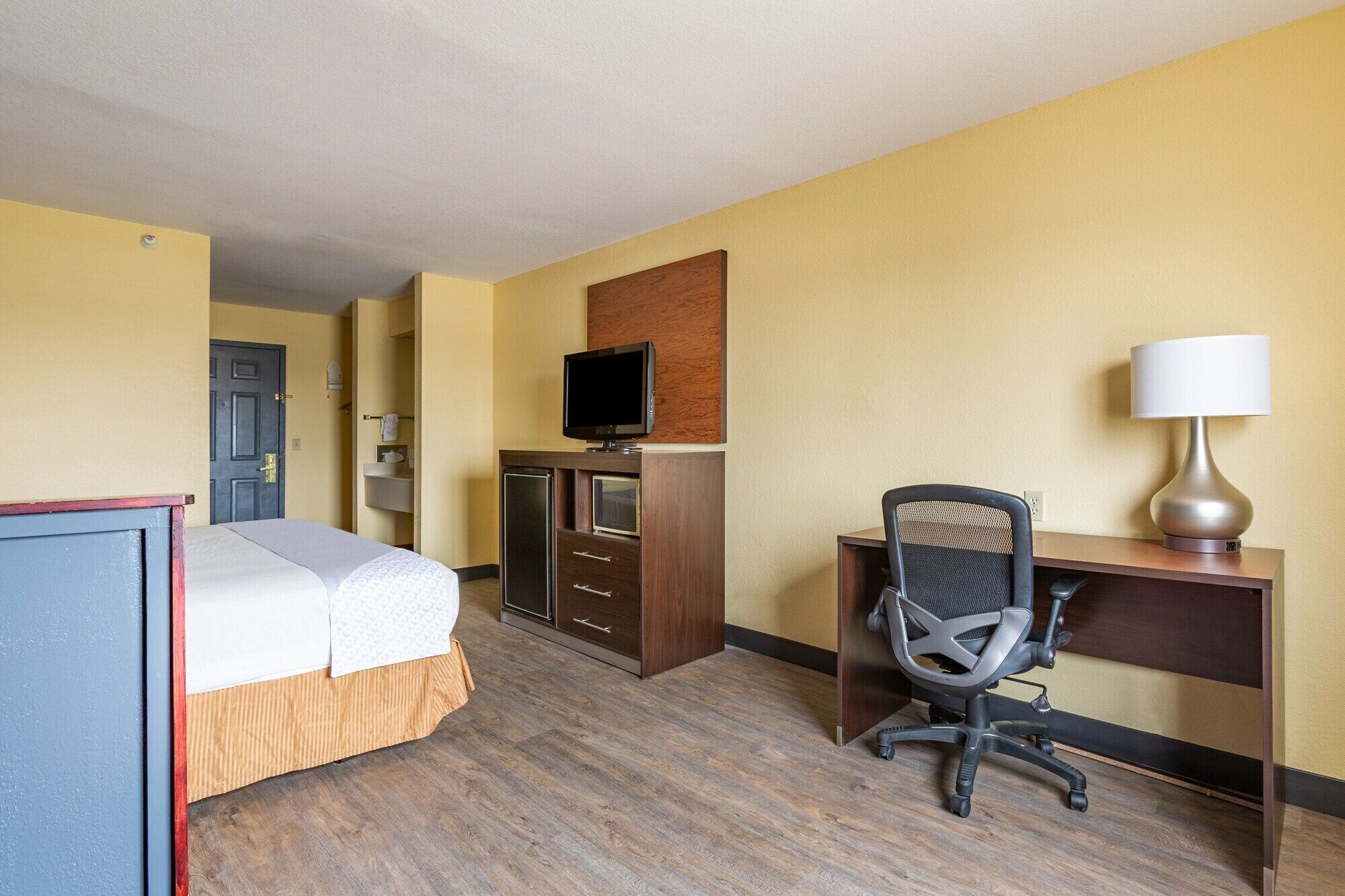 Una habitación de hotel con una cama, un escritorio con silla, un televisor y una lámpara.