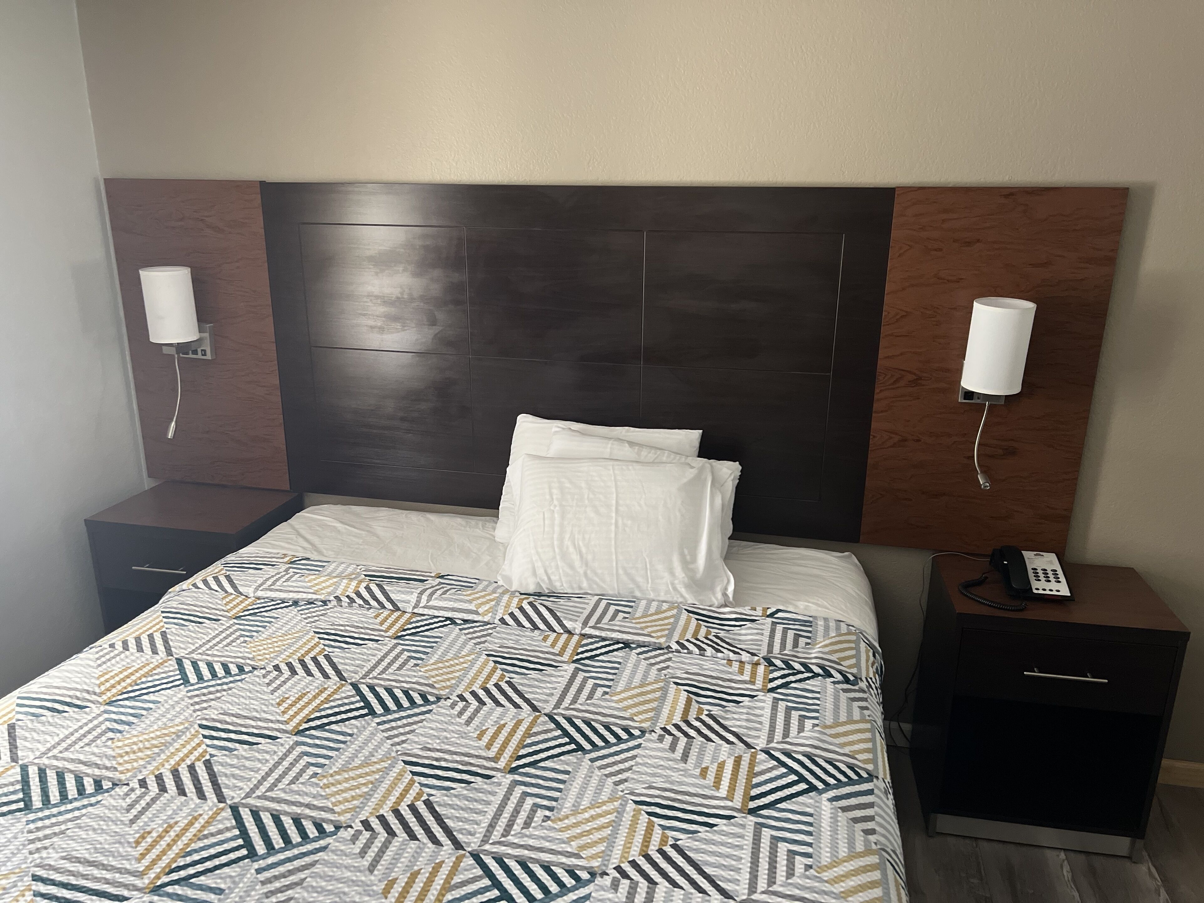 A hotel room with a large bed, a headboard, two bedside tables, and a telephone.