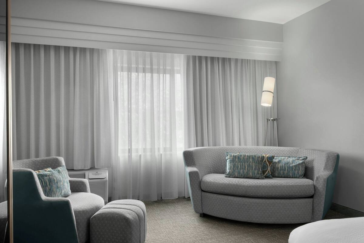 A modern hotel room with a grey sofa, a matching armchair, and a small side table.
