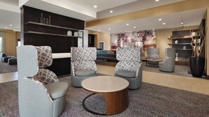 Eine moderne Lobby mit grau gemusterten Sesseln, einem runden Holztisch und einer großen Wandmalerei.