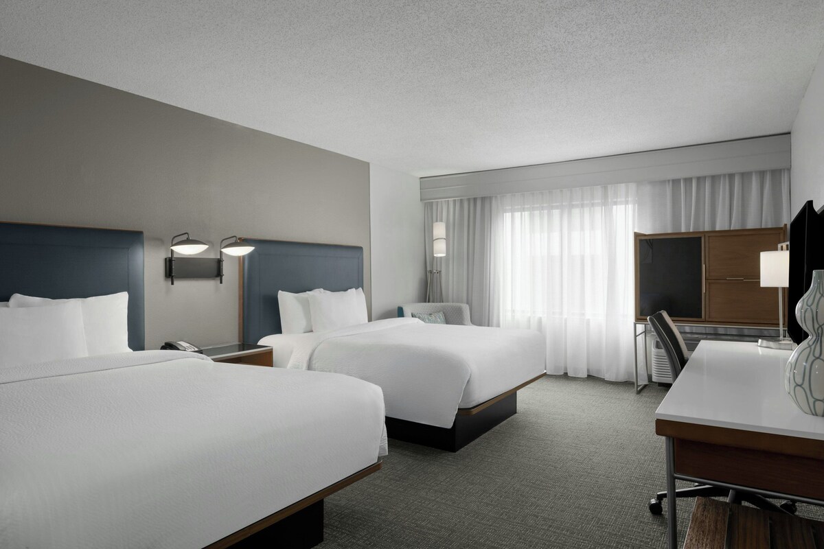 Ein Hotelzimmer mit zwei Betten, einem Schreibtisch und einem Stuhl.