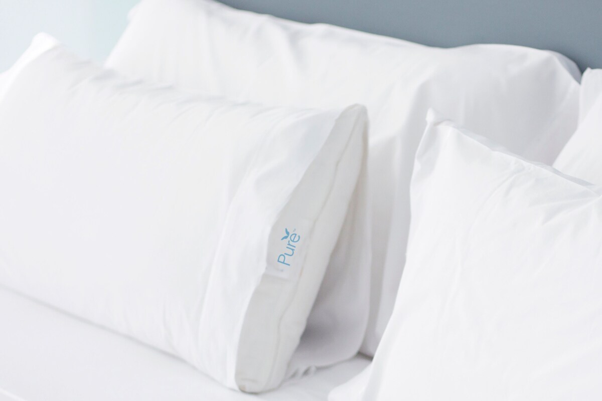 Una cama blanca con almohadas, una de ellas con la etiqueta que dice "Pure".