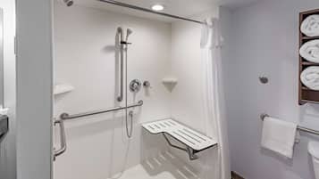 Un baño moderno con cabina de ducha, barras de apoyo, un toallero blanco y un estante con toallas.