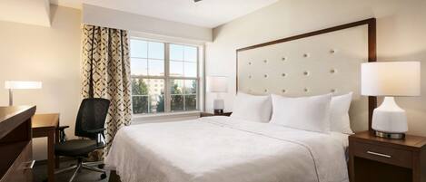 A hotel room with a large bed, a desk with a chair, a ceiling fan, and a window with curtains.