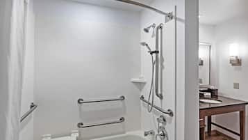 A modern bathroom with a white bathtub, grab bars, a shower with a handheld showerhead, and a vanity with a sink and mirror.