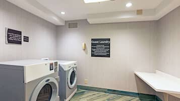 A laundry area with two washing machines, a sign indicating guest laundry, and a bench.