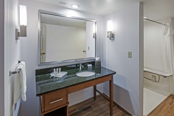 Un baño moderno con lavamanos de encimera de granito, un espejo grande y un mueble de tocador de madera.