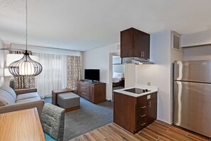 A modern hotel room with a kitchenette, a sofa, a TV, and a dining area.
