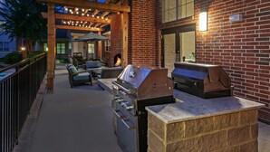 An outdoor patio with a brick wall, a wooden pergola, and a grill area.