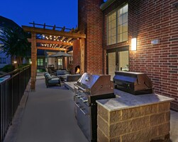 An outdoor patio with a brick wall, a wooden pergola, and a grill area.