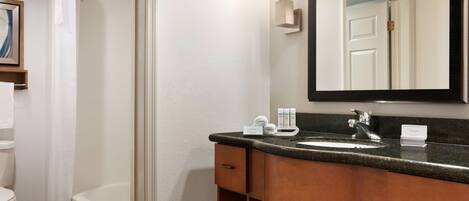 A modern bathroom with a shower, toilet, and bathtub. It includes a sink with toiletries and a mirror.