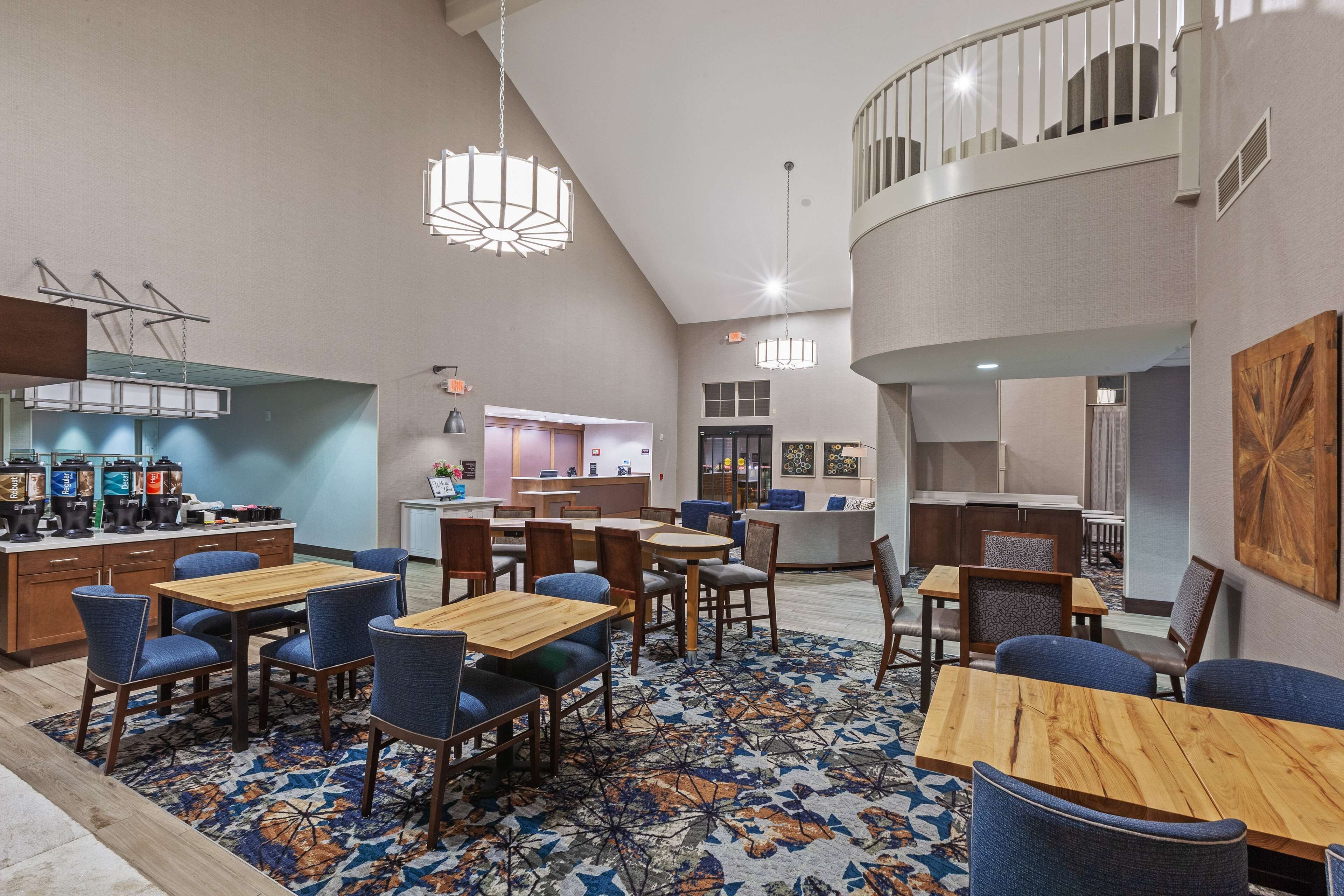 Een hotel lobby met een centrale zithoek, een bar en een trap naar een hoger niveau.