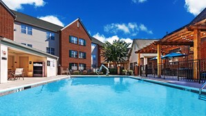 A swimming pool with clear blue water, surrounded by brick buildings with multiple windows and a covered patio area.