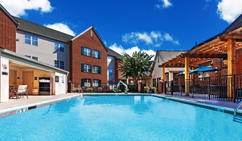 Una piscina con agua azul cristalina, rodeada de edificios de ladrillo con numerosas ventanas y un área de patio techada.