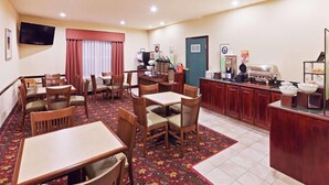 A hotel dining area with wooden tables and chairs, a buffet counter, and a television mounted on the wall. - Country Inn & Suites by Radisson, Tulsa, OK (Tulsa)