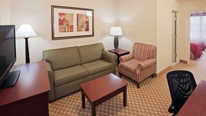 A hotel room with a green sofa, a striped armchair, a small wooden table, a TV, and two lamps. - Country Inn & Suites by Radisson, Tulsa, OK (Tulsa)