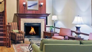 A cozy living room with a fireplace, a green sofa, striped armchairs, and a wooden staircase. - Country Inn & Suites by Radisson, Tulsa, OK (Tulsa)