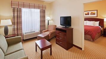 Quarto de hotel com cama, televisão, escrivaninha, cadeira e sofá.