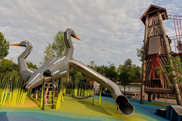 Un parque infantil con una gran escultura abstracta que representa a dos aves con cuellos extendidos y un tobogán.