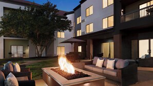 Un patio al aire libre con una chimenea, muebles de mimbre y un edificio al fondo.