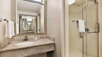 Une salle de bain dotée d’un lavabo avec un plan de toilette en granit, d’un miroir et d’une douche à parois de verre.