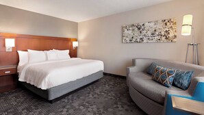 Habitación de hotel con cama, sofá, lámpara y una obra de arte en la pared.