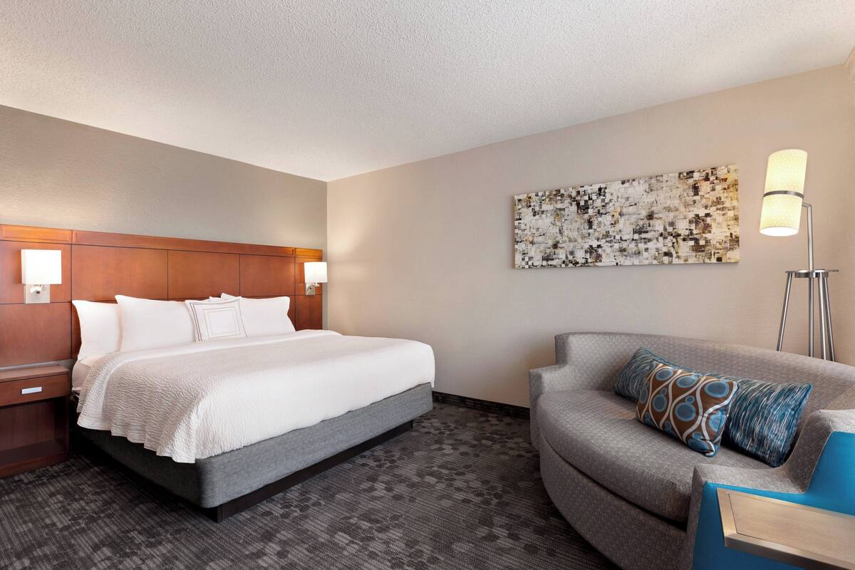 A hotel room with a bed, a sofa, a lamp, and a wall art piece.