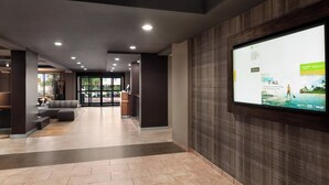 Un vestíbulo moderno con una gran pantalla digital mostrando un anuncio, una recepción y una zona de estar con un sofá y una mesa de centro.