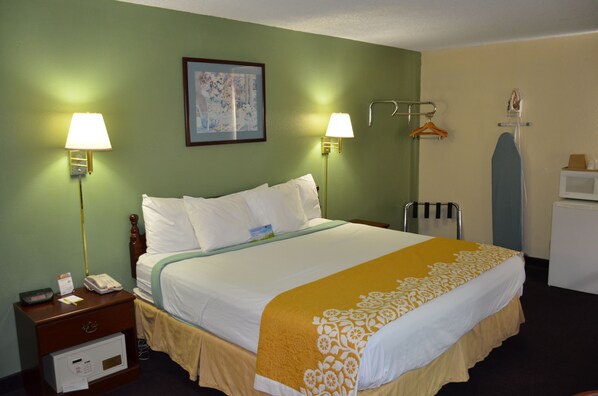 A hotel room with a bed, two bedside lamps, a framed picture on the wall, an ironing board, and a microwave.