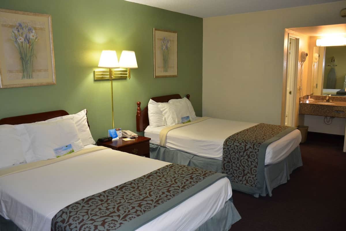 Une chambre d’hôtel avec deux lits, une table de chevet avec une lampe, une salle de bain avec un miroir et des œuvres d’art accrochées aux murs.