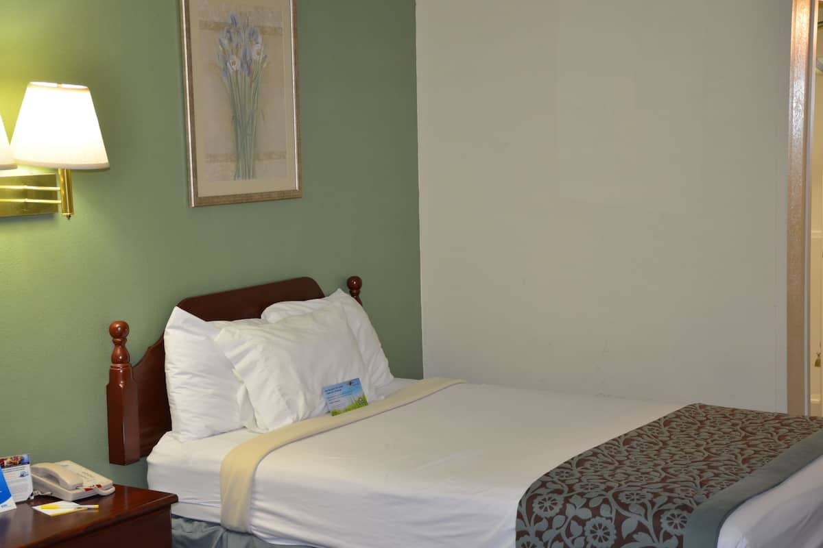 A hotel room with a bed, a nightstand with a lamp, a framed picture on the wall, and a door.