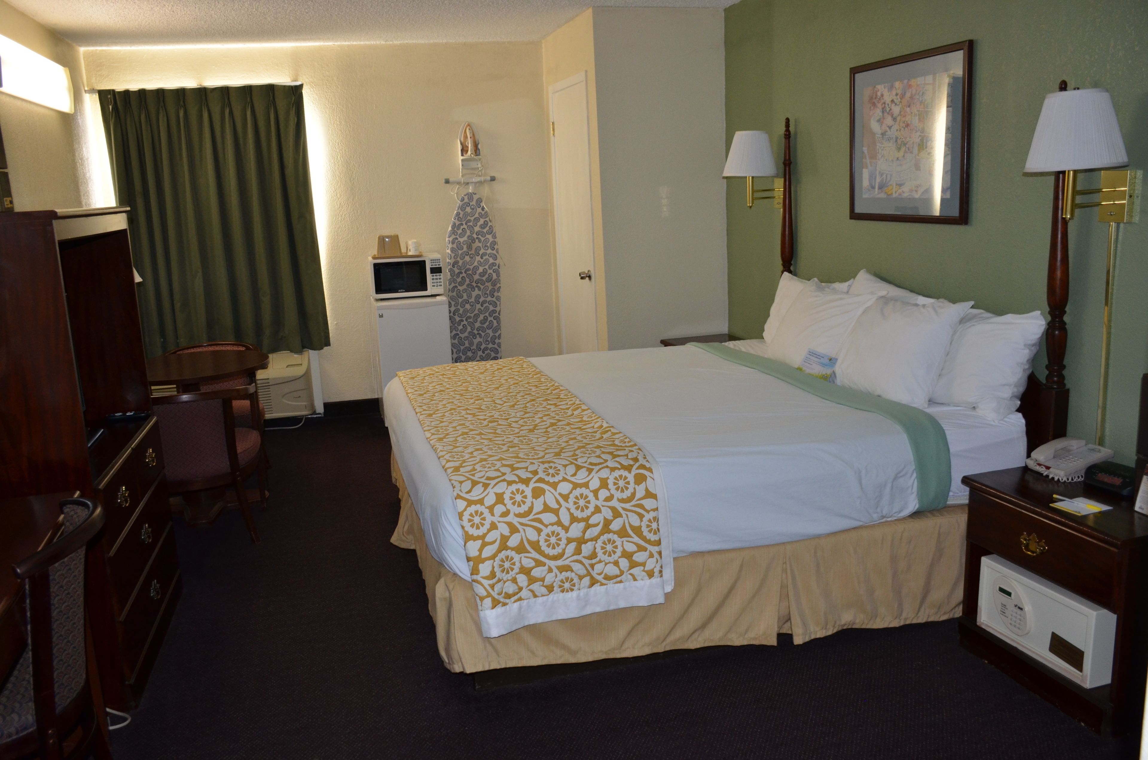 A hotel room with a bed, a desk, a chair, a microwave, a telephone, and a lamp.