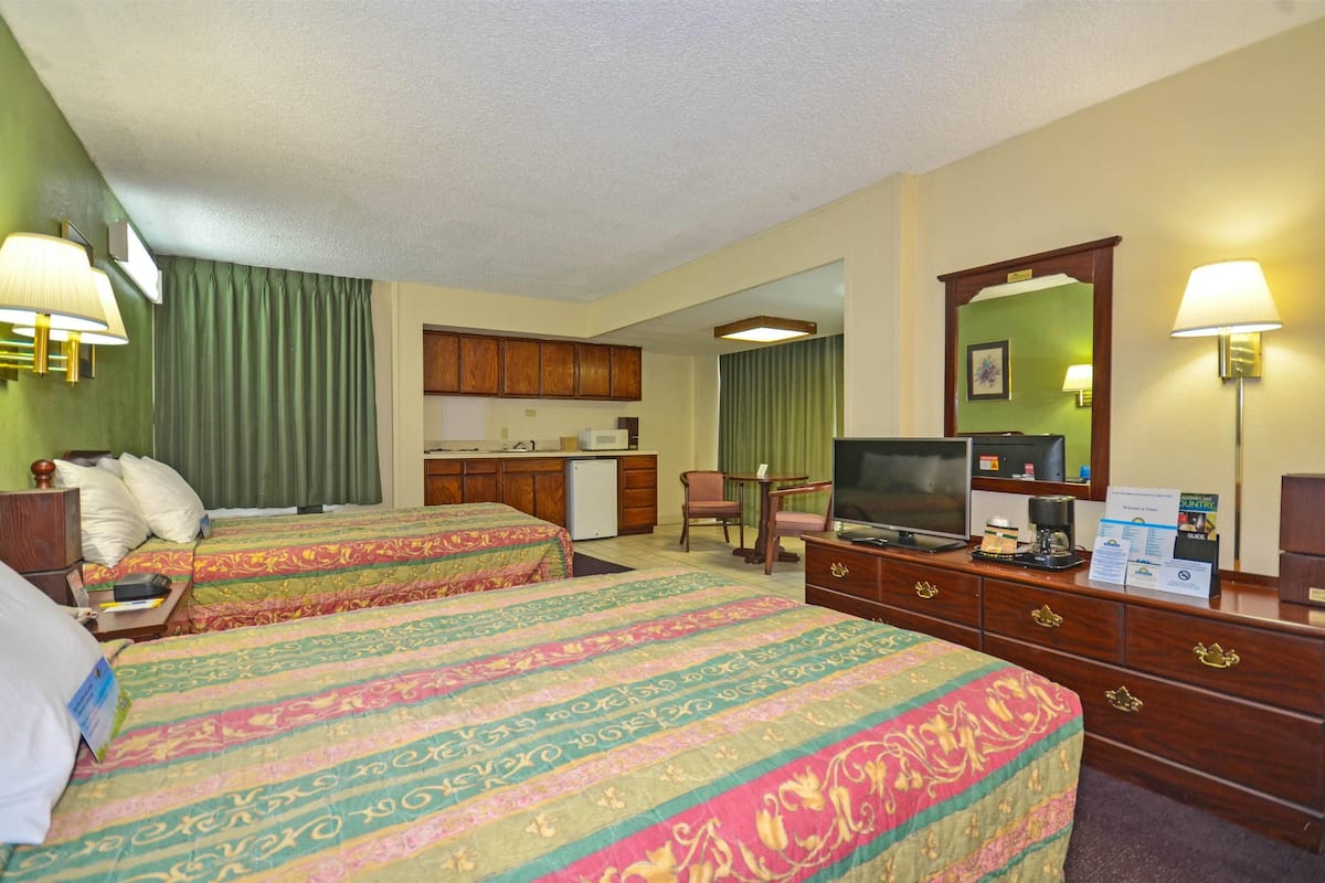 A hotel room with two beds, a television, a desk, and a kitchenette.