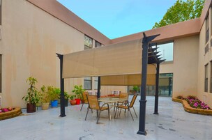 Un patio al aire libre con una mesa y sillas, rodeado de plantas en macetas y una pérgola.