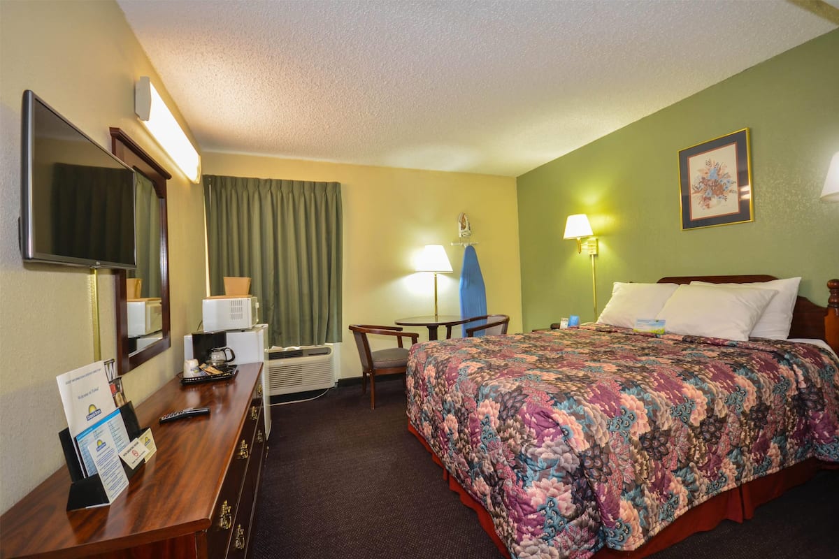 A hotel room with a bed, desk, chair, television, and a lamp.