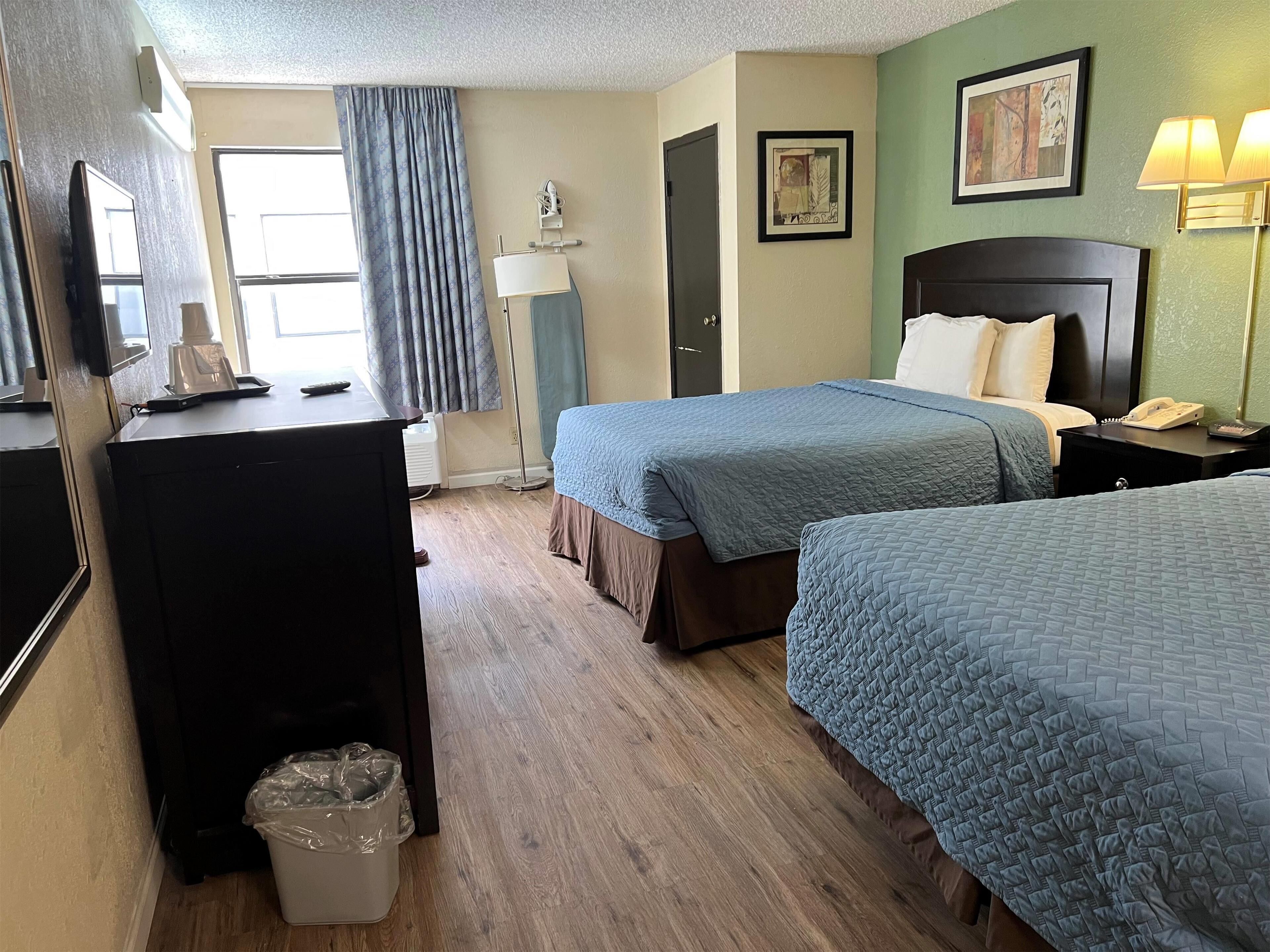 A hotel room with two beds, a desk, a lamp, and a trash bin.