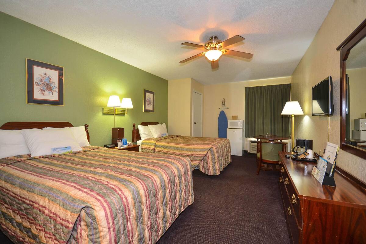 A hotel room with two beds, a desk, a chair, a television, and a ceiling fan.