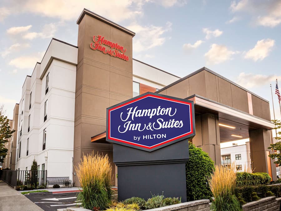 Näkyvässä paikassa sijaitseva Hampton Inn & Suites by Hilton -hotellin rakennus, jossa on suuri kyltti, parkkipaikka ja lippu.