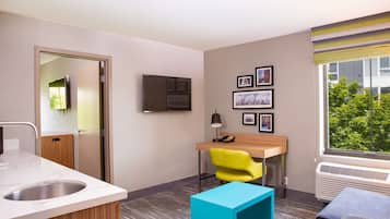 Habitación de hotel con baño, escritorio con silla, televisor y ventana con vistas a árboles.