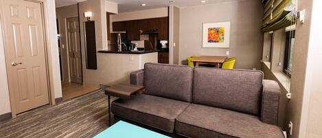 A modern living room with a gray sofa, a teal coffee table, and a kitchen in the background.