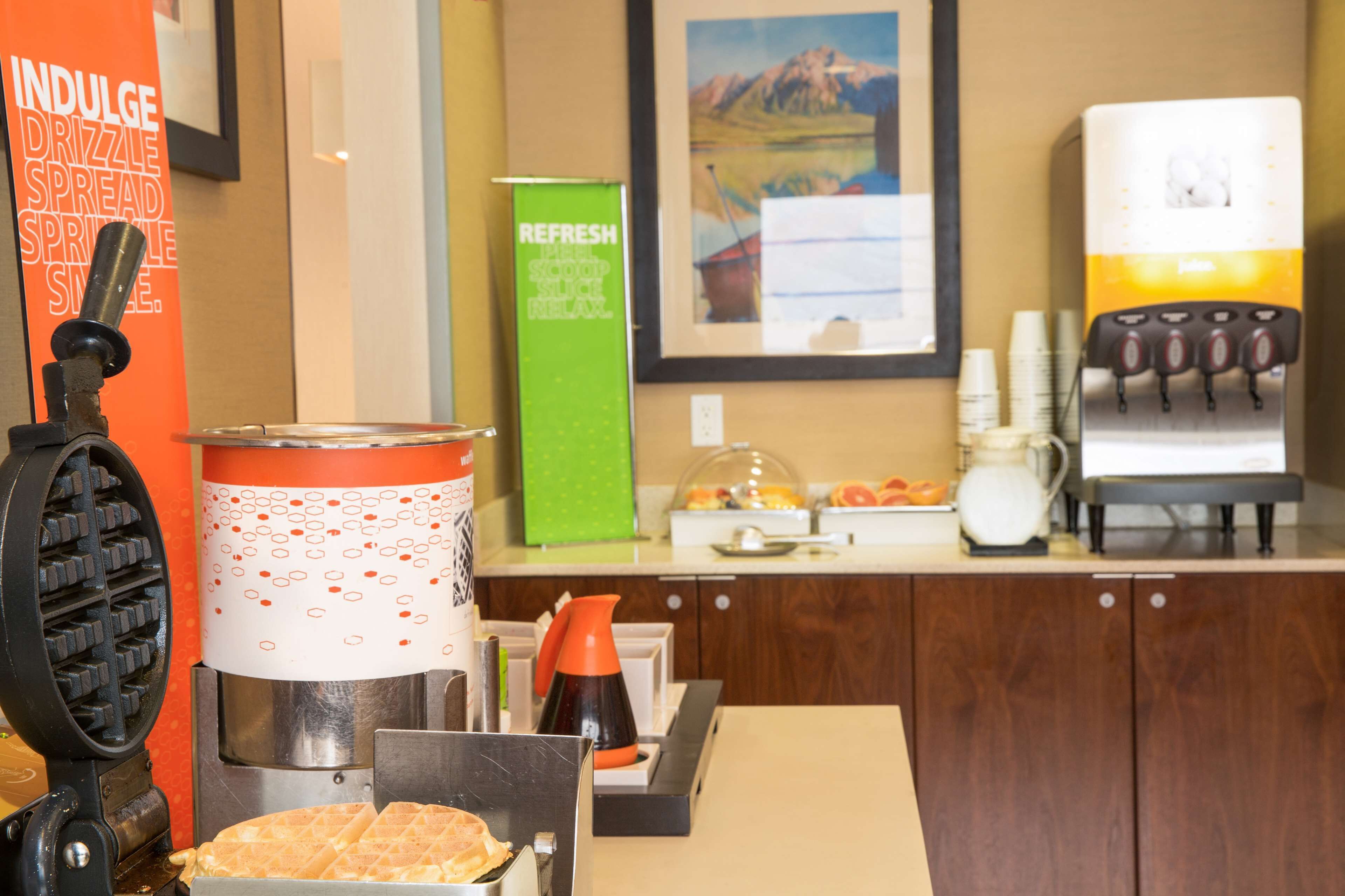 Uma área de cozinha com máquinas de waffle, cafeteira e dispensador de bebidas.