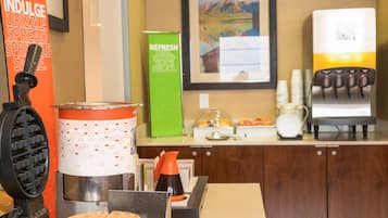 Uma área de cozinha com máquinas de waffle, cafeteira e dispensador de bebidas.