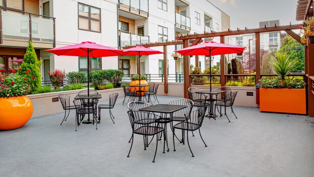 An outdoor patio area with tables and chairs, red umbrellas, and potted plants. - Hampton Inn & Suites Seattle-Downtown (Seattle)
