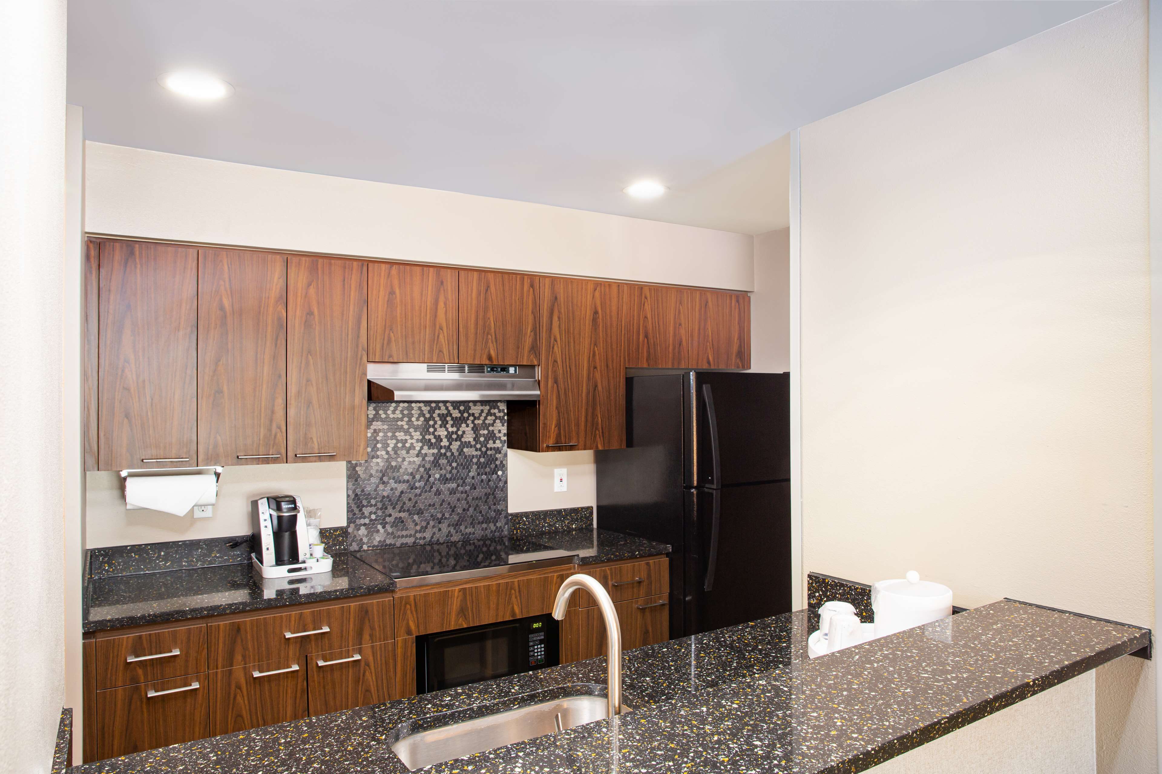 A modern kitchen with wooden cabinets, a stainless steel sink, a black refrigerator, and a coffee maker.