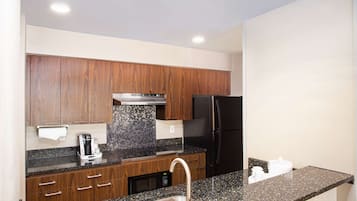 A modern kitchen with wooden cabinets, a stainless steel sink, a black refrigerator, and a coffee maker.