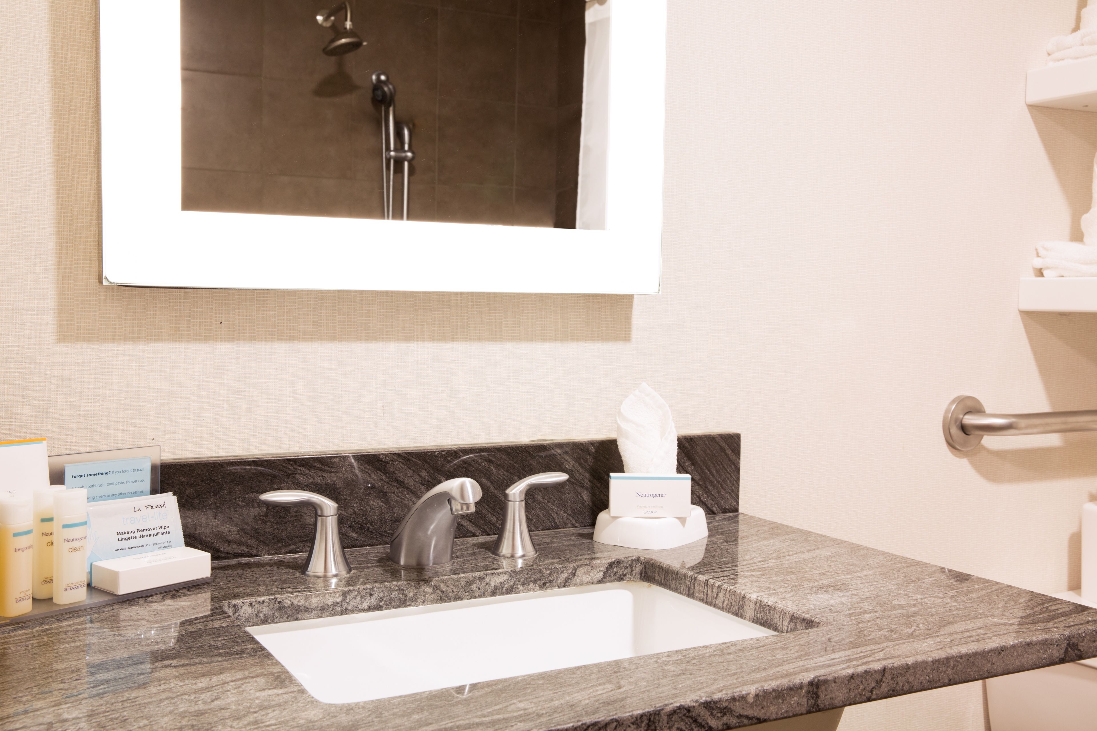 Un baño con encimera de mármol, un lavabo blanco y un espejo encima. Hay artículos de aseo y una caja de pañuelos en la encimera.