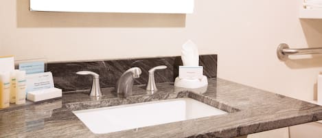 Un baño con encimera de mármol, un lavabo blanco y un espejo encima. Hay artículos de aseo y una caja de pañuelos en la encimera.
