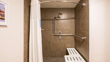 A shower with a handheld showerhead, grab bars, and a white shower seat.