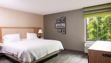 Habitación de hotel con cama, escritorio, ventana con vista a árboles y cuadros en la pared.